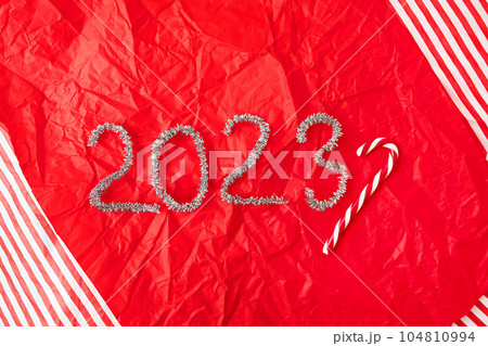 Lettering 2023 from glittering garland rain on red gift wrapping paper background. New Year and Christmas decor, Christmas candy on the background. Lettering 2023 from glittering garland rain on red gift wrapping paper background. New Year and Christmas decor, Christmas candy on the background. 104810994