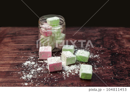 Colored candies in the form of oriental sweets neatly folded in a glass jar and laid out on a wooden table Colored candies in the form of oriental sweets neatly folded in a glass jar and laid out on a wooden table 104811453