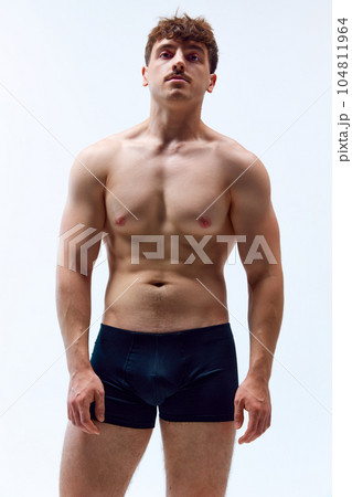 Portrait of handsome young man with mustache, posing shirtless in underwear against grey studio background. Muscular, sportive body Portrait of handsome young man with mustache, posing shirtless in underwear against grey studio background. Muscular, sportive body 104811964