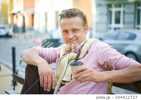 Street food concept of man enjoying tasty cup of coffee on bench outdoors. Aroma and flavor of coffee add to sensory experience of urban delight. Man's relaxed posture create sense of ease and leisure Street food concept of man enjoying tasty cup of coffee on bench outdoors. Aroma and flavor of coffee add to sensory experience of urban delight. Man's relaxed posture create sense of ease and leisure 104812727