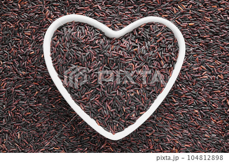 Pile of brown rice with heart shaped bowl, top view 104812898