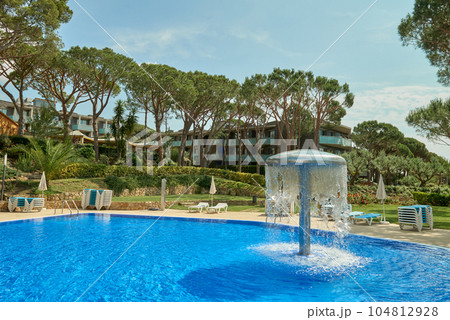 Relaxation swimming pool in a leisure camp. Empty Swimming pool with waterfall jet. Pool side on summer sunny day. Seaside vacation and hotel resort concept. Reflection in blue clean sea water pool Relaxation swimming pool in a leisure camp. Empty Swimming pool with waterfall jet. Pool side on summer sunny day. Seaside vacation and hotel resort concept. Reflection in blue clean sea water pool 104812928