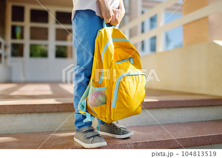 Little student with a backpack on the steps of the stairs of school building. Close-up of child legs, hands and schoolbag of boy standing on staircase of schoolhouse.Back to school concept. 104813519