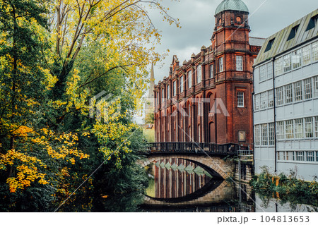 Brick bridge over the river with medieval and industrial buildings and yellow trees background. Norwich City in autumn. Commercial Estate near River In Europe. 104813653