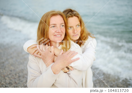 Redhead senior mother and her beautiful adult daughter are walking together and embracing. Family relationships between adult children and older parents Redhead senior mother and her beautiful adult daughter are walking together and embracing. Family relationships between adult children and older parents 104813720