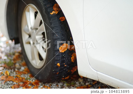 White automobile is in the mountains on autumn day. Wheel of car on gravel road with fallen leaves stuck to it. Road trip in european Alps. Travel and tourism. White automobile is in the mountains on autumn day. Wheel of car on gravel road with fallen leaves stuck to it. Road trip in european Alps. Travel and tourism. 104813895