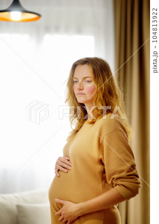 Pregnant caucasian woman relaxing at home. Young expectant mother strokes her pregnant belly and thinks about the baby childbirth. Concept of motherhood and pregnancy 104813922