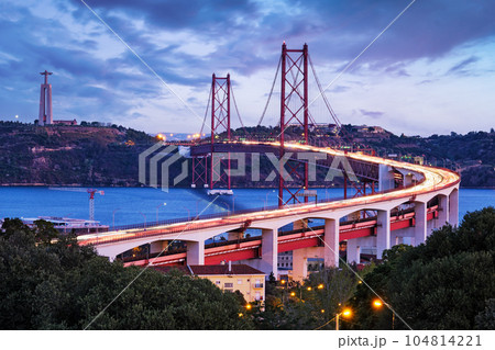View of Lisbon view from Miradouro do Bairro do Alvito viewpoint of Tagus river, traffic with light trails on 25th of April Bridge, and Christ the King statue in the evening twilight. Lisbon, Portugal View of Lisbon view from Miradouro do Bairro do Alvito viewpoint of Tagus river, traffic with light trails on 25th of April Bridge, and Christ the King statue in the evening twilight. Lisbon, Portugal 104814221