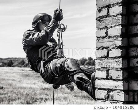 Silhouette of police officer in tactical gear descending from a height, rope exercises with weapons. Tactical rappelling, anti-terror or counter terrorism operation in darkness in rappelling harness Silhouette of police officer in tactical gear descending from a height, rope exercises with weapons. Tactical rappelling, anti-terror or counter terrorism operation in darkness in rappelling harness 104815586