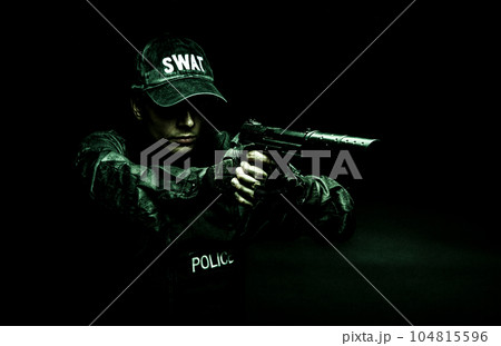 Spec ops police officer SWAT in black uniform aiming pistol with silencer, studio shot, half length 104815596