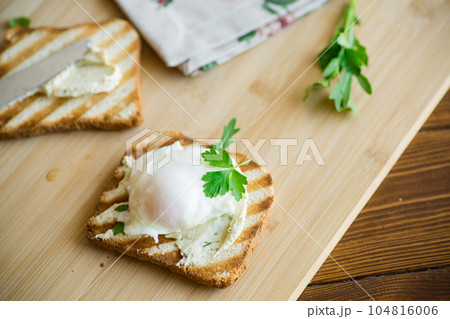 Fried toast bread with spread and poached egg, on a wooden table. 104816006