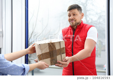 Emotional courier giving damaged cardboard box to client in doorway, closeup. Poor quality delivery 104816593