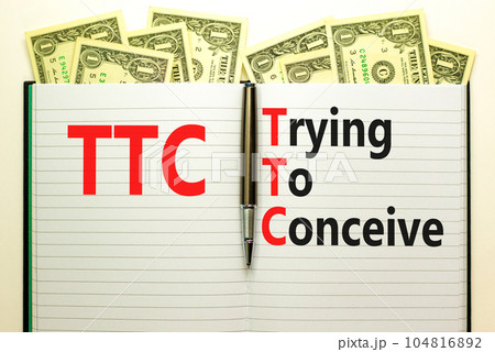 TTC trying to conceive symbol. Concept words TTC trying to conceive on white note on a beautiful background from dollar bills. Pen. Medical and TTC trying to conceive concept. Copy space. 104816892