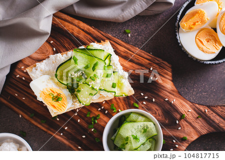 Close up of sandwich with ricotta, cucumber slices, boiled egg and sesame seeds on a board top view Close up of sandwich with ricotta, cucumber slices, boiled egg and sesame seeds on a board top view 104817715