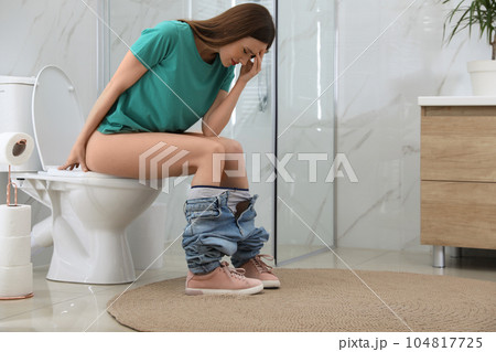 Woman suffering from hemorrhoid on toilet bowl in rest room 104817725