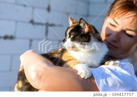 Woman holds a pet cat against the background of a built house. Woman holds a pet cat against the background of a built house. 104817757