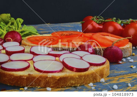 Spread butter on bread with sliced tomatoes and radishes. Fresh snack on natural wooden background Spread butter on bread with sliced tomatoes and radishes. Fresh snack on natural wooden background 104818973