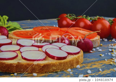 Spread butter on bread with sliced tomatoes and radishes. Fresh snack on natural wooden background 104818974