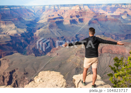 Young hiker is standing on a steep cliff taking in the amazing view over famous Grand Canyon on a beautiful sunny day with blue sky in summer, Grand Canyon National Park, Arizona, USA 104823717