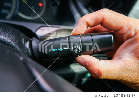 The driver hand turns on the fog lamp switch in the car. The driver hand turns on the fog lamp switch in the car. 104824147