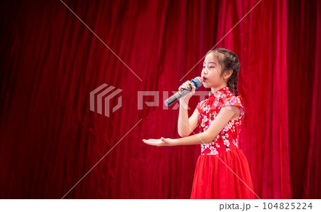 The Asian kid girl sing a song on stage at her school activity day, dress in Qipao style, red curtain background The Asian kid girl sing a song on stage at her school activity day, dress in Qipao style, red curtain background 104825224