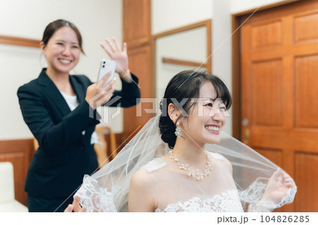 結婚式・披露宴の準備をするウェディングドレスを着た花嫁・新婦とスマホで写真を撮るプランナーの女性 結婚式・披露宴の準備をするウェディングドレスを着た花嫁・新婦とスマホで写真を撮るプランナーの女性 104826285