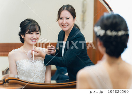 ブライズルーム・控え室で花嫁・新婦にメイクをするブライダルヘアメイクアーティストの女性（リップ） 104826560