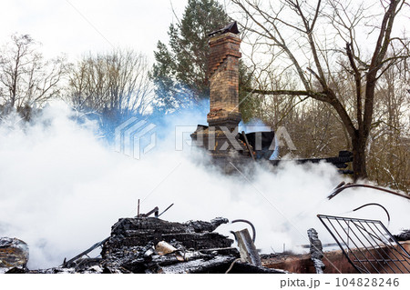 Smoke on the ashes, brick chimney in smoke after a fire in a wooden building 104828246