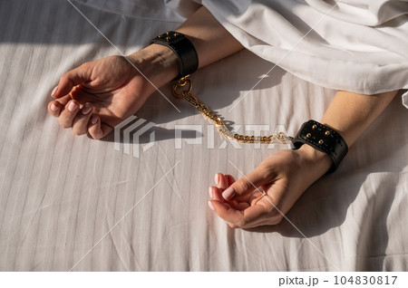 Close-up of woman's hands in leather handcuffs. Sex toy. Close-up of woman's hands in leather handcuffs. Sex toy. 104830817