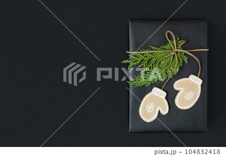 Black craft gift box with paper mittens and cedar tree branches on dark background with space for your text Black craft gift box with paper mittens and cedar tree branches on dark background with space for your text 104832418