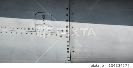 Silver metal surface of the aircraft fuselage with rivets. Fuselage detail view. Airplane metallic fuselage detail with rivets. 104834173
