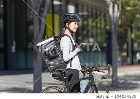 スマホを手に持ってロードバイクを引いているフードデリバリー 女性配達員 スマホを手に持ってロードバイクを引いているフードデリバリー 女性配達員 104834529