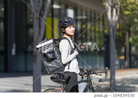 スマホを手に持ってロードバイクを引いているフードデリバリー 女性配達員 スマホを手に持ってロードバイクを引いているフードデリバリー 女性配達員 104834530