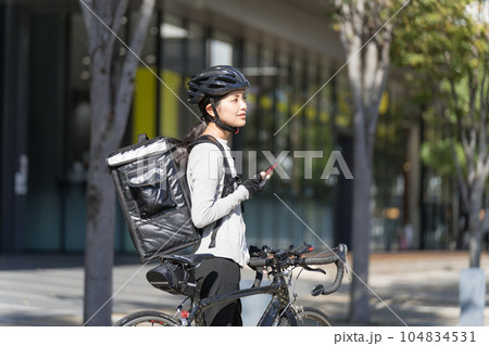 スマホを手に持ってロードバイクを引いているフードデリバリー 女性配達員 スマホを手に持ってロードバイクを引いているフードデリバリー 女性配達員 104834531