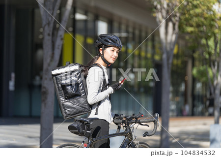 スマホを手に持ってロードバイクを引いているフードデリバリー 女性配達員 スマホを手に持ってロードバイクを引いているフードデリバリー 女性配達員 104834532
