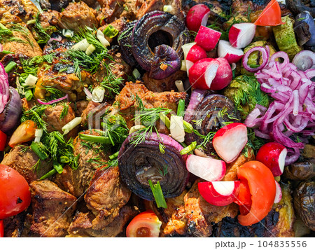 Shish kebab with vegetables in the open air. Grilled meat with fresh tomatoes, onions, radishes and herbs 104835556