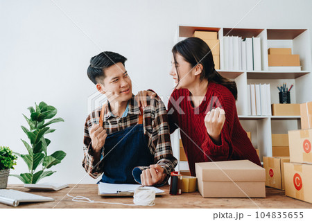 A young Asian couple shows delight and smiles on their faces when they see the sales volume and customer orders exceed expectations. sme or small business family concepts. A young Asian couple shows delight and smiles on their faces when they see the sales volume and customer orders exceed expectations. sme or small business family concepts. 104835655