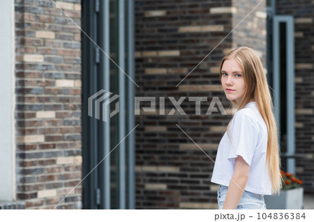 young woman enters the door of a city building against a blurred urban background 104836384