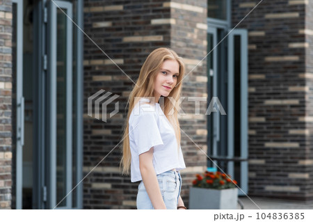 young woman stepped out of the door of a city building against a blurred urban background 104836385