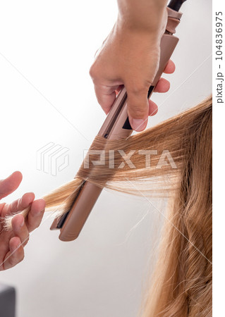 Hair stylist prepares woman makes curls hairstyle with curling iron. Hair stylist prepares woman makes curls hairstyle with curling iron. 104836975