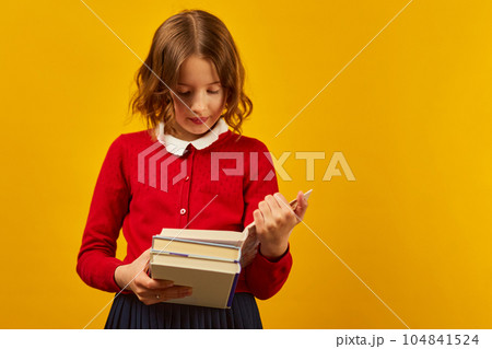 Portrait of happy schoolgirl reading a book on yellow studio 104841524