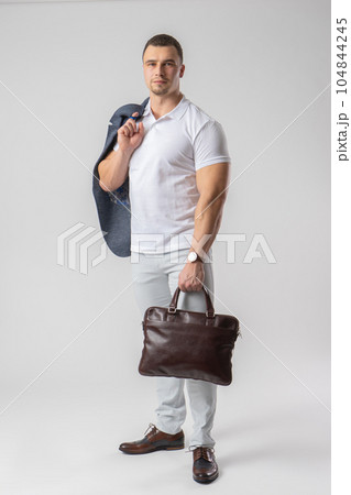 A man in casual clothes holds a leather briefcase and a jacket in his hands. A man in casual clothes holds a leather briefcase and a jacket in his hands. 104844245