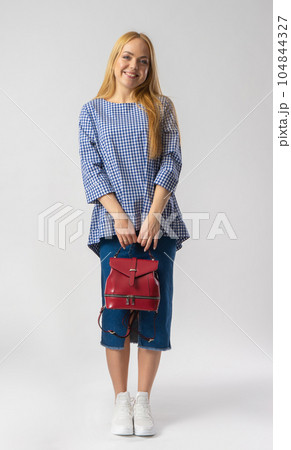 A blonde woman in casual clothes holds a backpack in her hands. 104844327