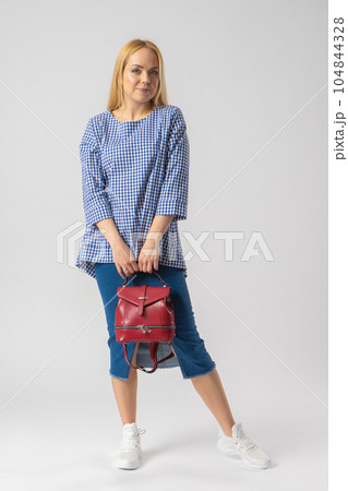 A blonde woman in casual clothes holds a backpack in her hands. A blonde woman in casual clothes holds a backpack in her hands. 104844328