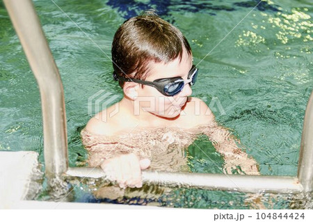 Boy in the indoor public pool. Portrait of child with swimmng goggles. Boy goes up on ladder. 104844424