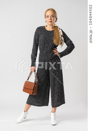 A woman in an elegant black suit with white polka dots, with a women's handbag. 104844502