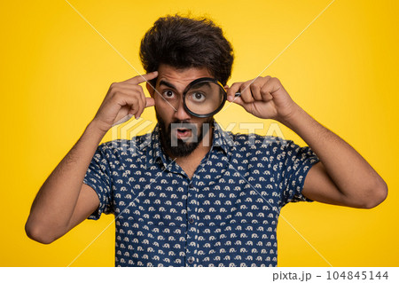 Investigator researcher man with magnifying glass near face, looking into camera with big zoom eye 104845144