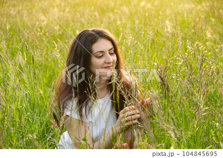 Young woman admiring the nature of field grass in summer. The unity of people and nature 104845695