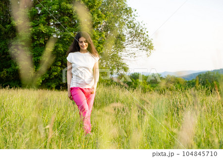 A young woman walks across a field. A walk in nature in the summer. 104845710