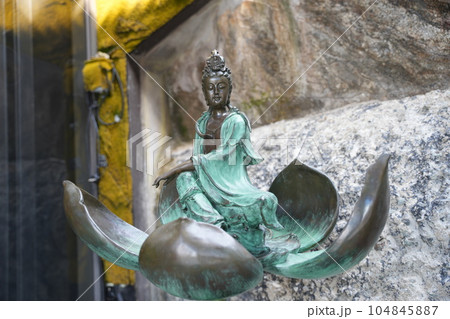 A faded Buddha sits in an antique position on a lotus flower. 104845887